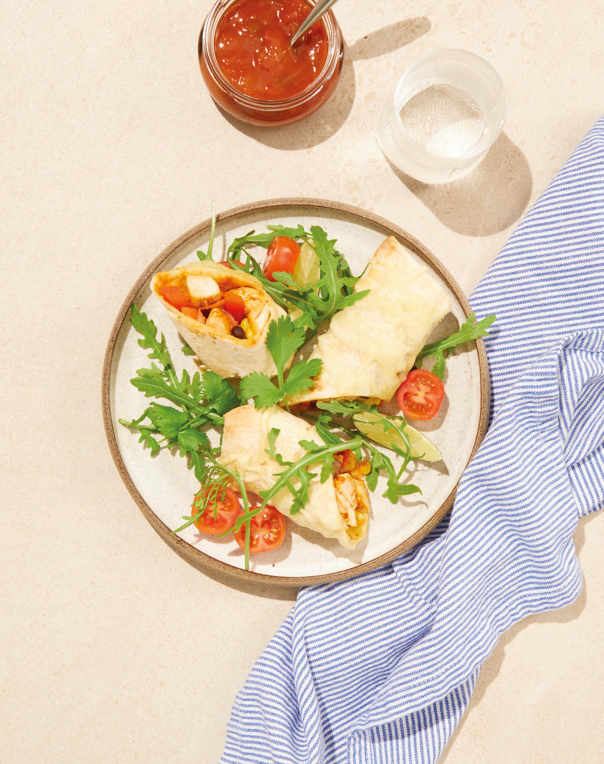 Gratinert burritos på tallerken med blått kjøkkenhåndle ved siden av. 