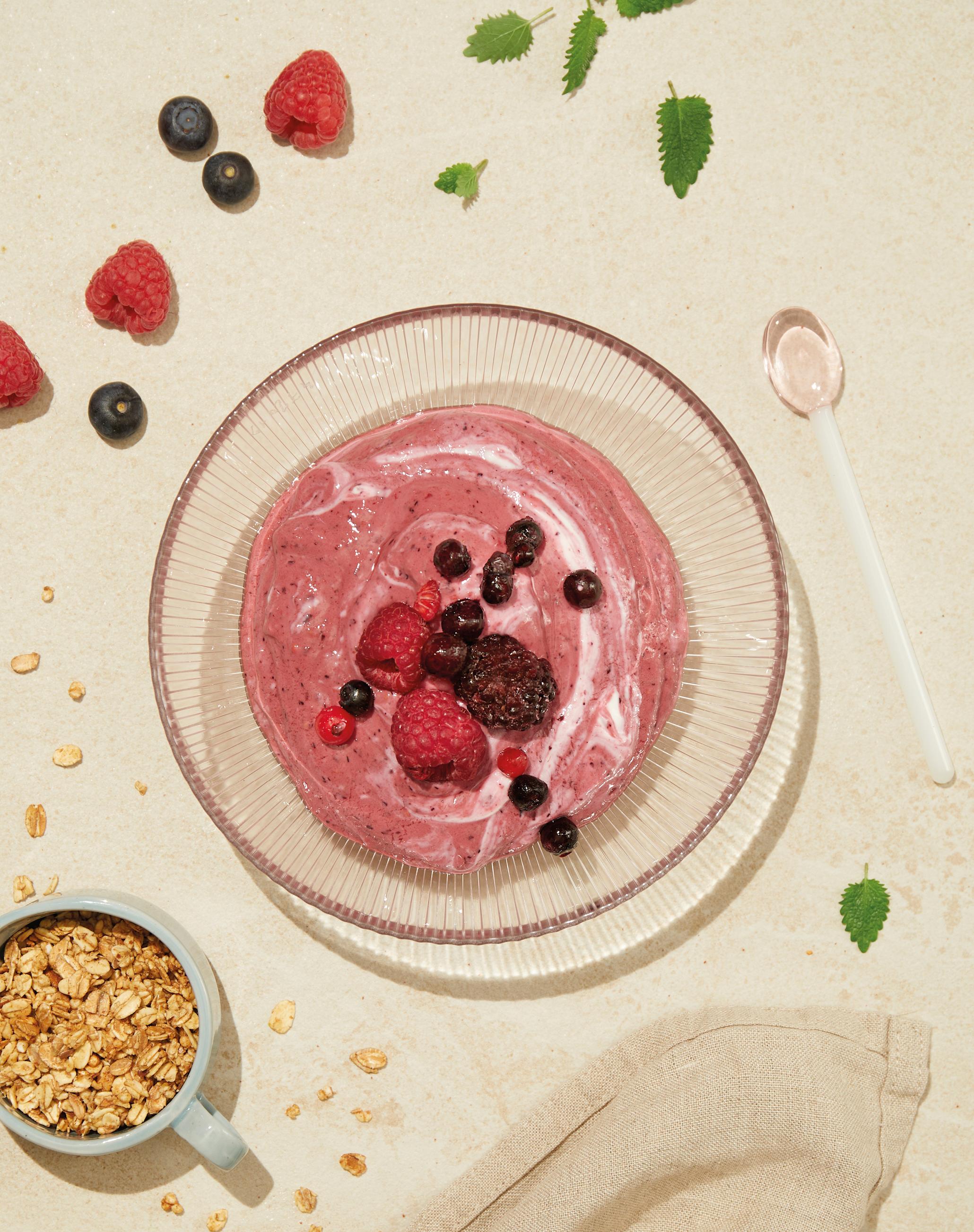 Rosa frozen yoghurt laget med bær, servert i gjennomsiktig skål, og toppet med bær.