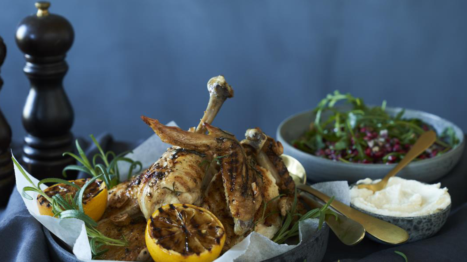 Grillet økologisk kylling på et fat med granateplesalat og fetakrem i skåler ved siden av.