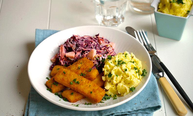 Stekte fiskepinner med coleslaw og potetmos på hvit middagstallerken. Lys blå linserviett under tallerkenen, og bestikk på siden.