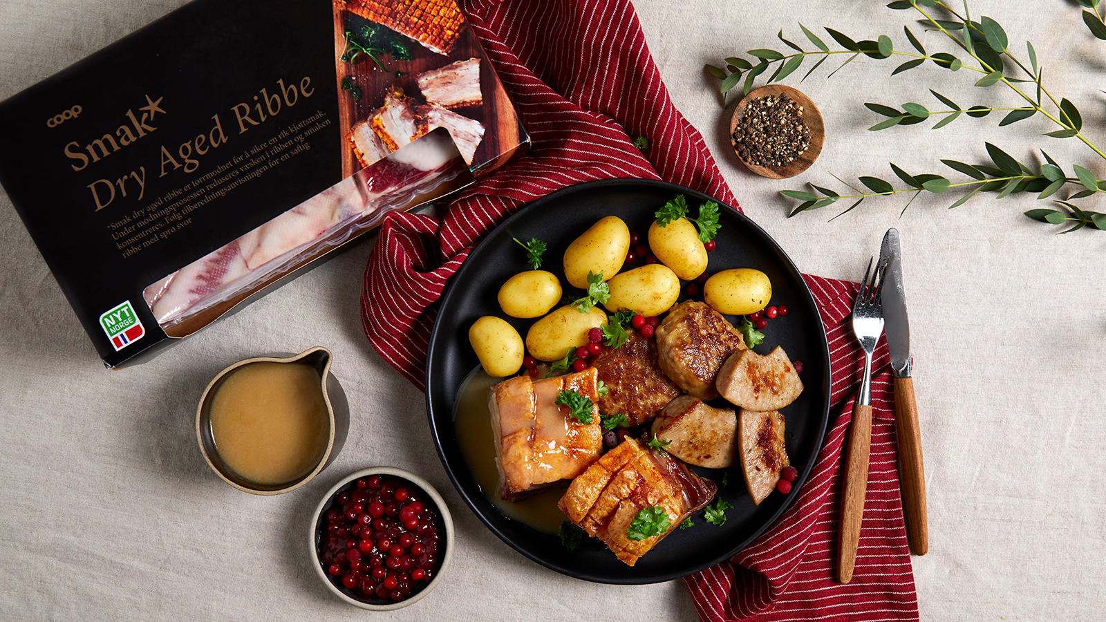 Langtidsstekt dry aged ribbe med ribbesaus servert på svart tallerken med medisterkaker, julepølse, dampede poteter, tyttebær og kruspersille.