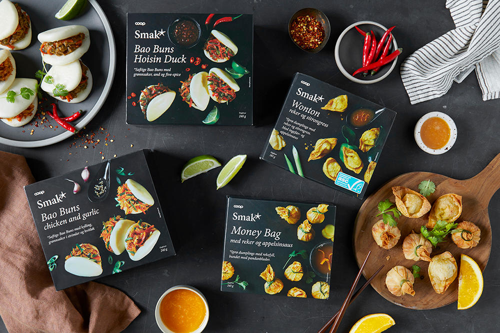 Smak* Bao buns hoisin duck og chicken and garlic, Smak* Wontons og Smak* Money bag i emballasje på svart bakgrunn, med tilberedte moneybags og bao buns på siden.