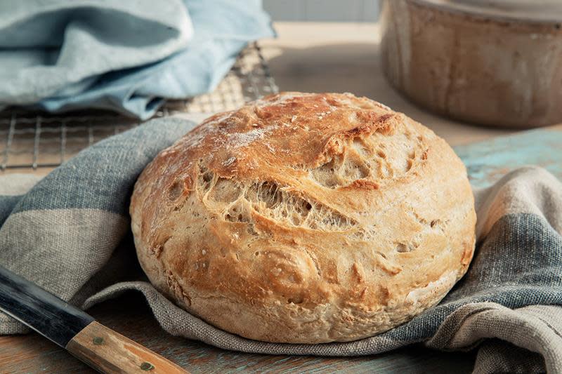Eltefritt brød med gyllen skorpe og meldryss servert på blåstripete rustikk kjøkkenhåndkle med brødkniv i forgrunn.