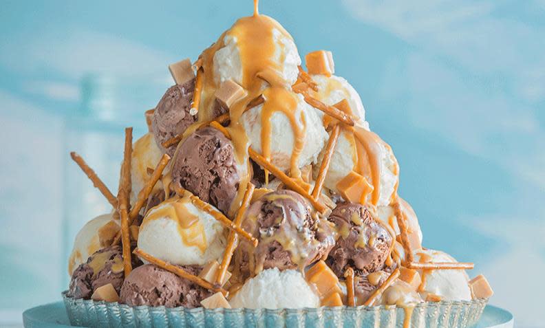 Iskremtårn med kuler av sjokoladeis og vaniljeis, hjemmelaget karamellsaus og saltstenger. Lys blå bakgrunn.