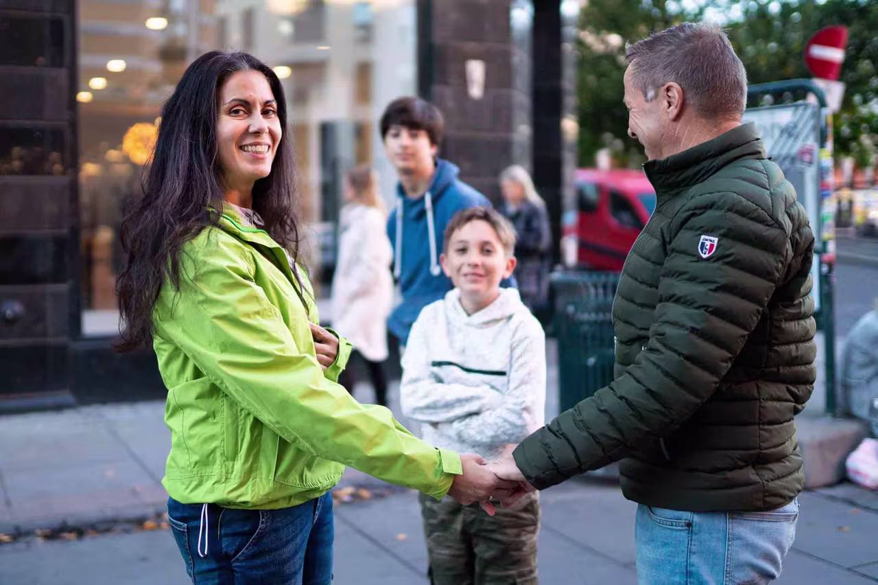 Mann og kone holder hender, barn smiler i bakgrunnen. 