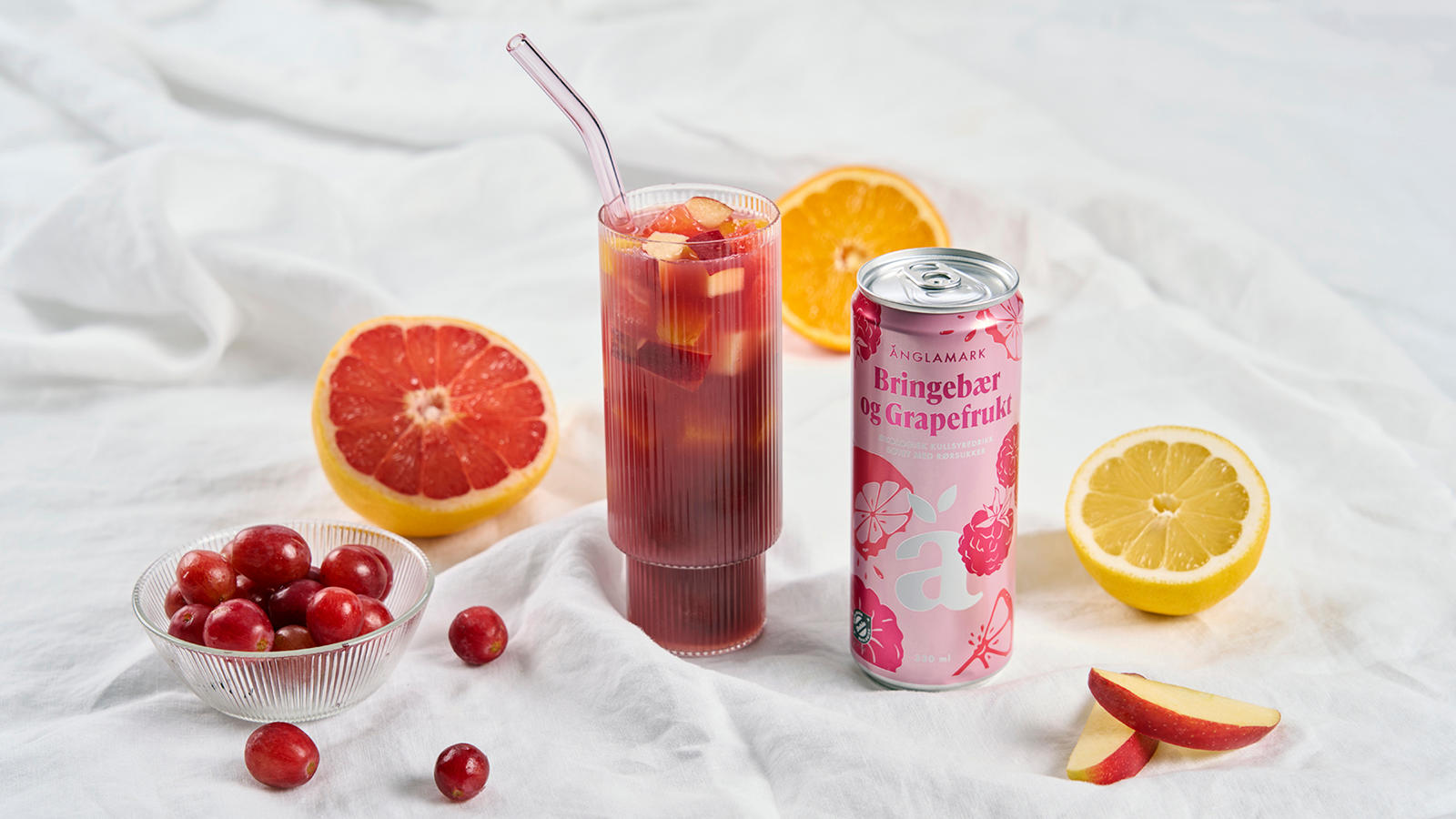 Alkoholfri Sangria servert i høyt glass med frisk frukt og frosne druer. Boks med Änglamark Bringebær og Grapefrukt ved siden av, og frisk sitrus rundt.