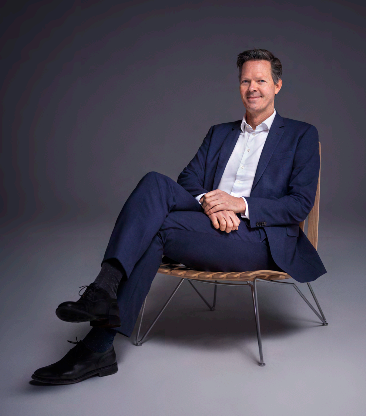 Philipp Engedal, administrerende direktør i Coop sitter med beina i kors på en stol i mørkeblå dress