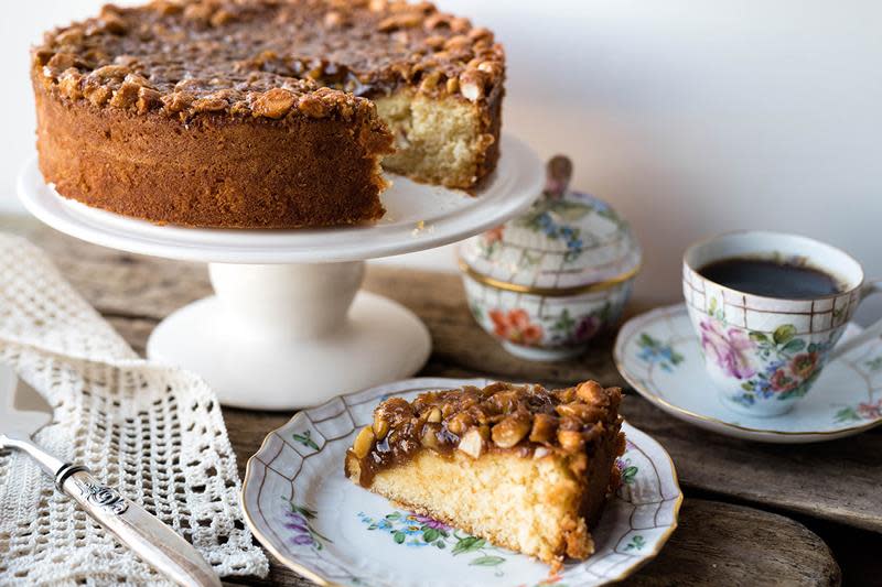 Saftig toscakake servert på hvitt stettfat, med et stykke toscakake servert på blomstrete kaffeservise på siden.