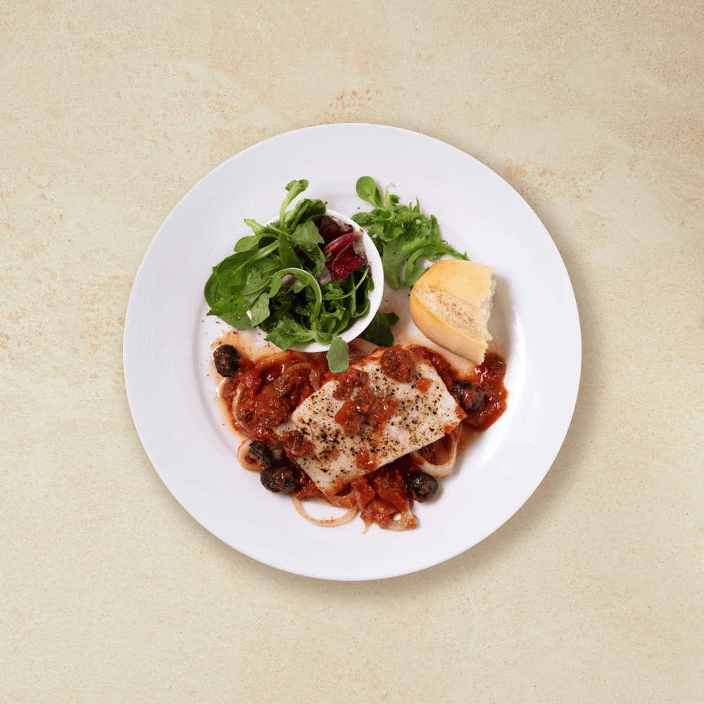 Torsk i form med tomat og oliven, servert på hvit middagstallerken med salatblanding og en bit lys baguette.