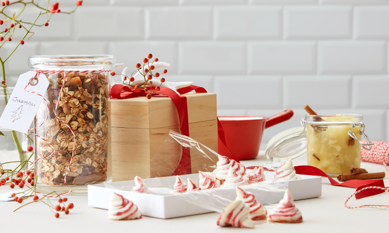 Julekrydret eplemos på glass, med kanelstang og stjerneanis, på bord med spiselige julegaver.