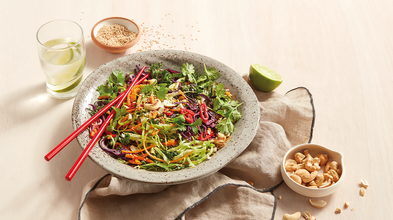 Spicy asiatisk råkostsalat, servert i lys bolle, med en skål cashewnøtter ved siden av.