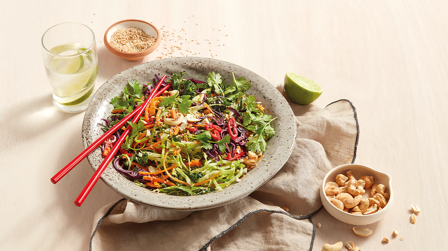 Spicy asiatisk råkostsalat, servert i lys bolle, med en skål cashewnøtter ved siden av.