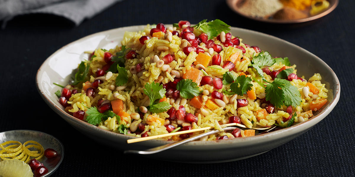 Arabisk machboos med gulrøtter, pinjekjerner og granateplefrø, servert i skål på mørk bakgrunn. Koriander på toppen.