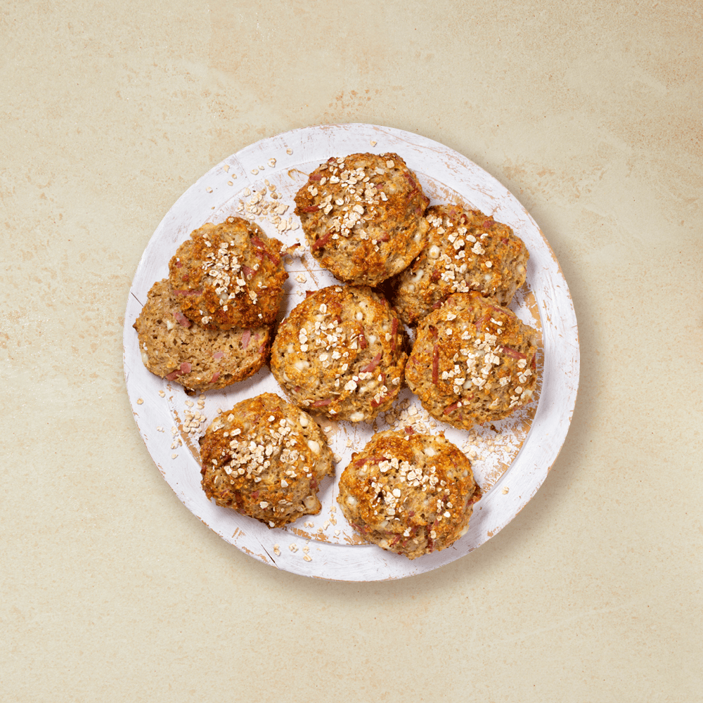 Proteinrundstykker med skinke og cottage cheese, servert med et dryss havregryn på toppen på et hvitt rundt trefat.