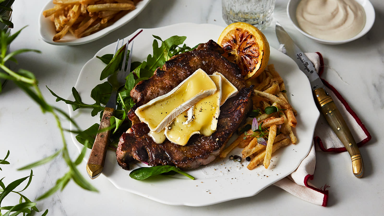 Entrecôte med lun brie servert med pommes frittes og hjemmelaget aioli på hvit tallerken med frisk salat og grillet sitron.