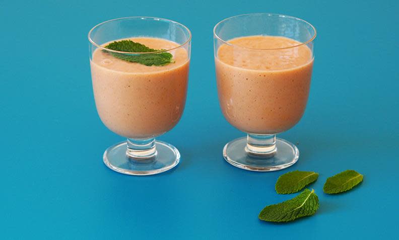 Favorittsmoothie med avokado, mynte og jordbær servert i to stettglass på blå bakgrunn med mynteblader ved siden av. Ett mynteblad på toppen av den ene smoothien.