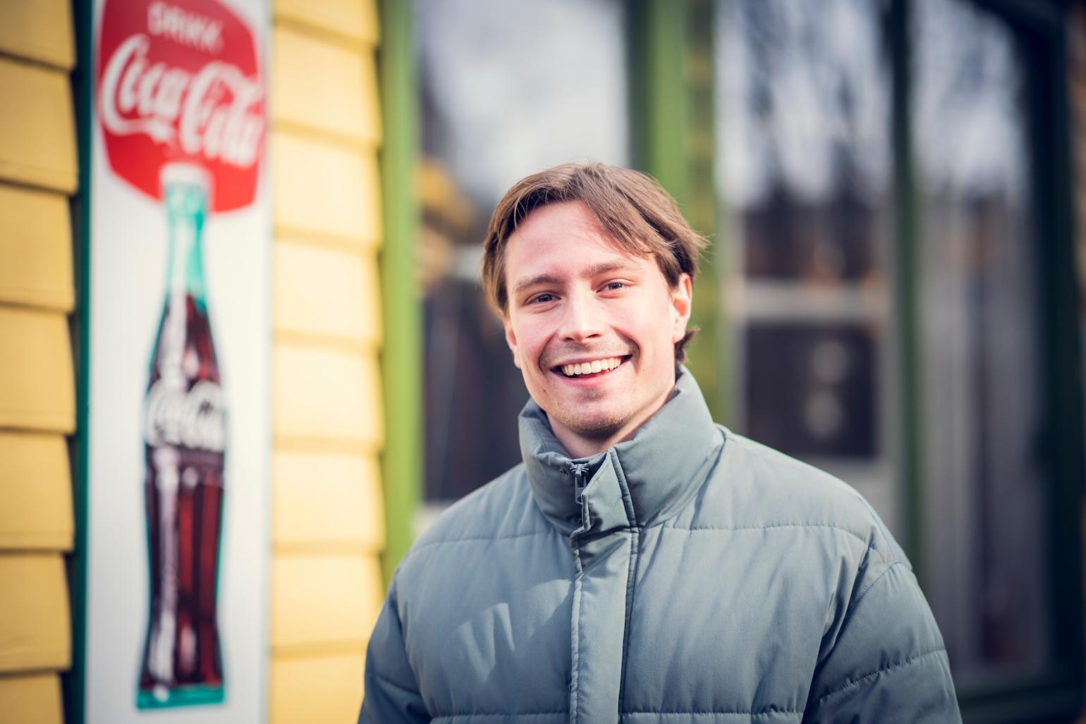 Smilen mann med et gammelt cola-skilt i bakgrunnen