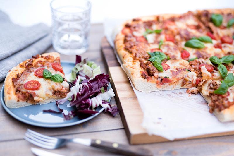Langpannepizza med kjøttdeig og tomater, toppet med fersk basilikum, servert på trefjøl.