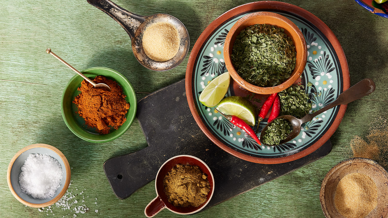 Hjemmelaget tacokrydder delt opp i ingredienser i flere små rustikke skåler. Limebåter og fersk rød chili som pynt.