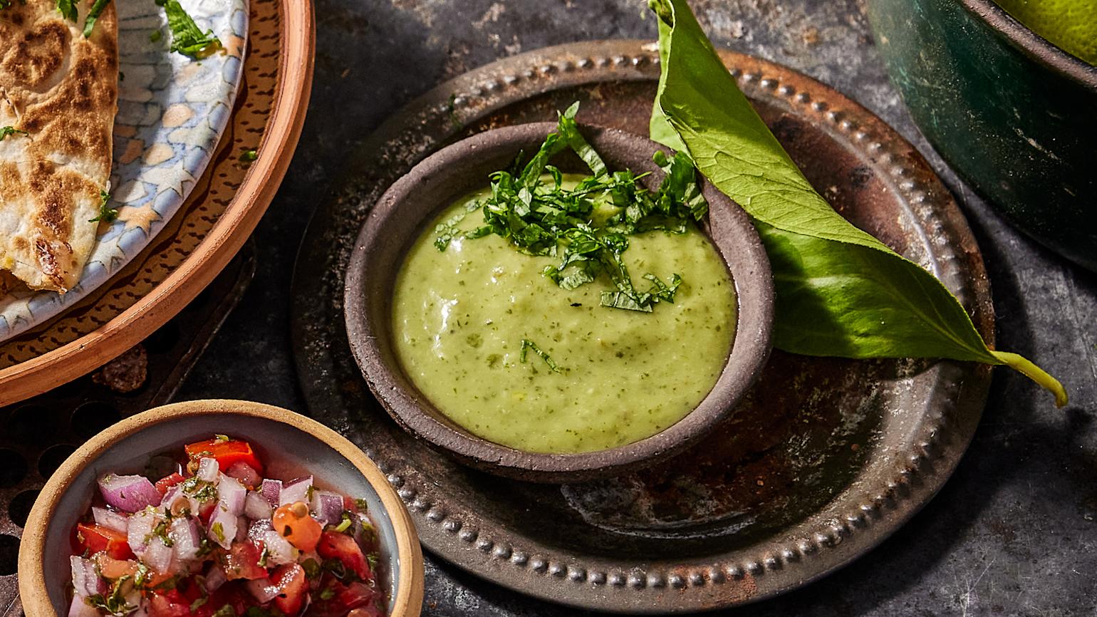 Grønn avokadosalsa servert i en liten skål og pyntet med hakket koriander. Liten skål med salsa ved siden av.