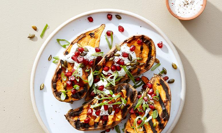 Grillet søtpotet, servert med creme fraiche, granateple og et dryss vårløk. Servert på hvit tallerken, på beige bakgrunn.