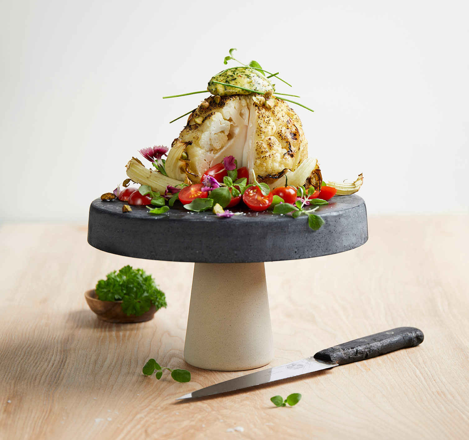 Hel grillet blomkål med estragonsmør, servert på fat med tomater og urter.