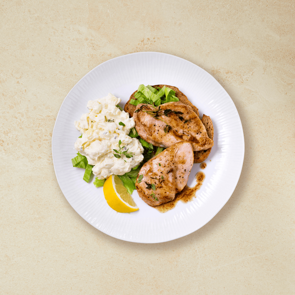 To stekte kyllingfileter på hvit tallerken, med ferdig potetsalat, strimlet salat og en sitronbåt.