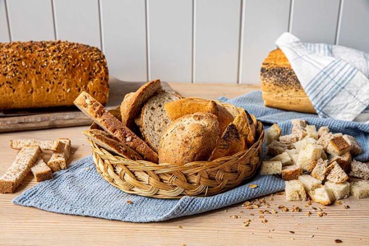 Rester av forskjellig typer brød, i både kurv og på skjærefjøl. Terninger av brød rundt kurven, og hele brød i bakgrunnen.