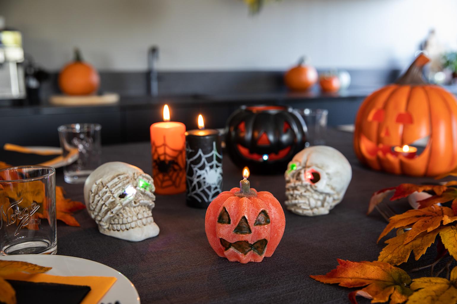 Et sort kjøkkenbord, dekket til Halloween, med gresskarlys, hodeskaller og høstblader.