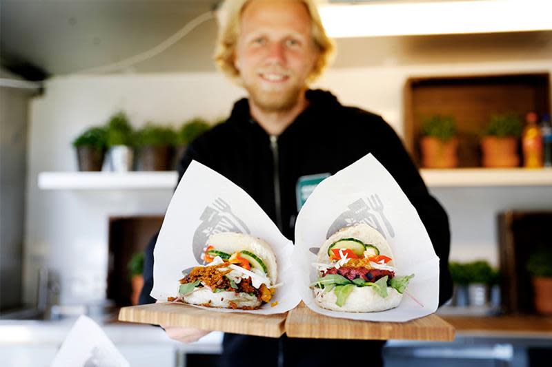 Mann holder fram to vegetarburgere med salat og grønnsaker. 
