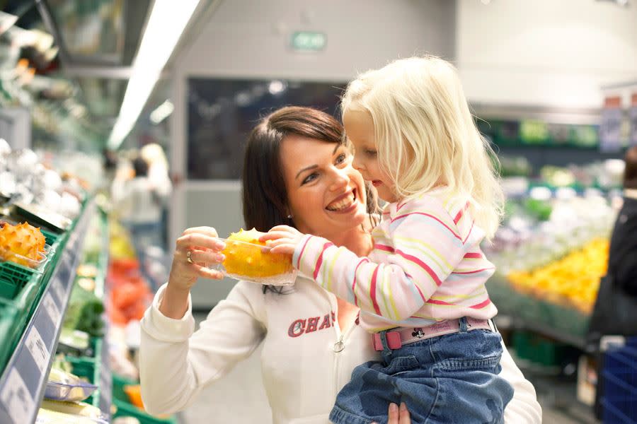 Dame og hennes unge datter i matbutikken. Datteren tar på en gul spiss frukt.