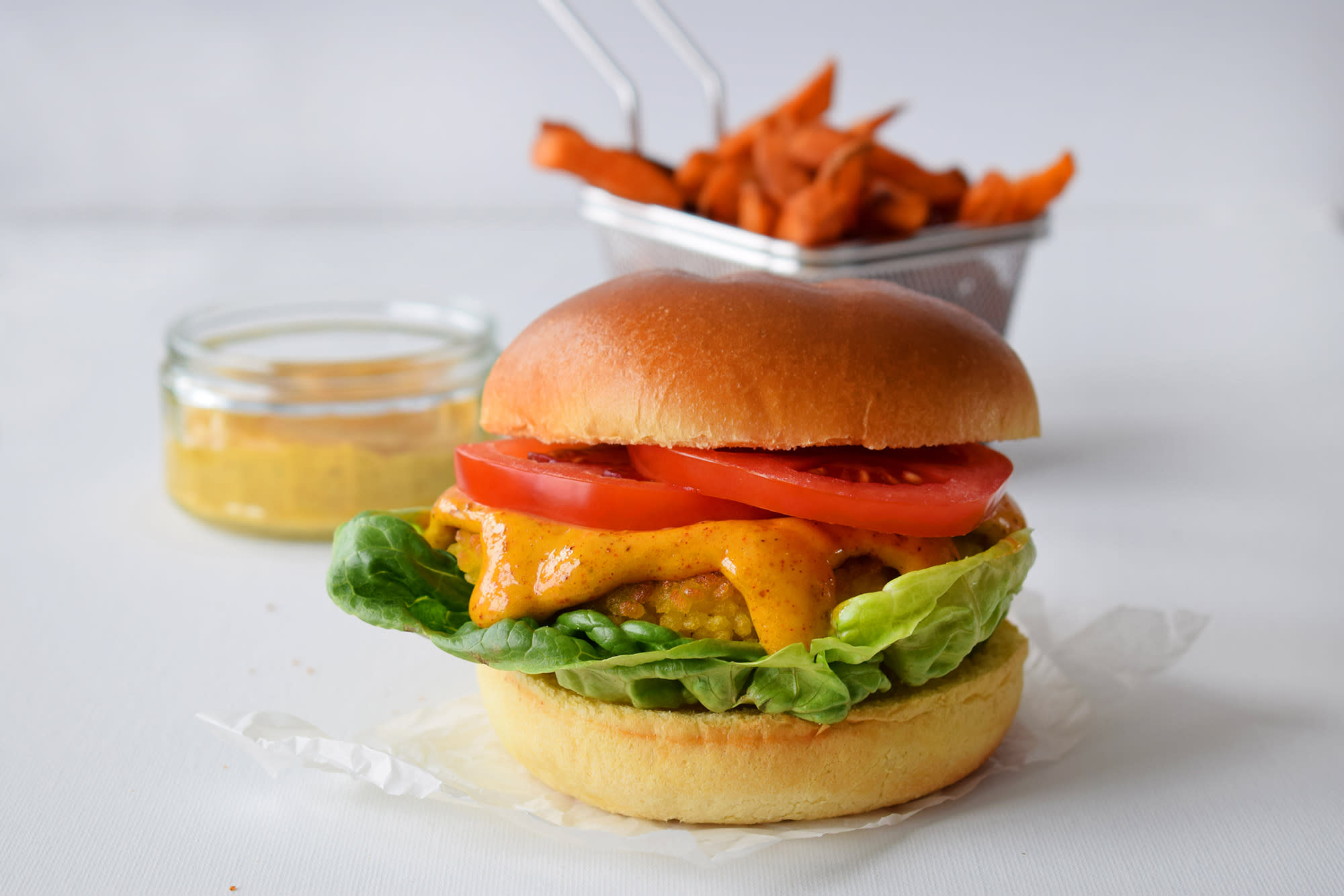 Crispy fiskeburger med ost, med hjemmelaget currymayo, tomatskiver og hjertesalat. Servert i burgerbrød, med søtpotetfries og et lite glass currymayo på siden.