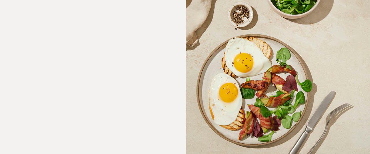 To toast med speilegg, bacon og basilikum på en tallerken på høyre side og beige bakgrunn på høyre side