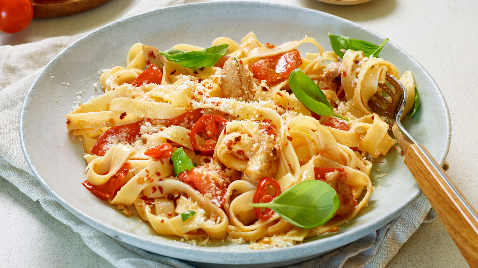 Fettucini med chili og kylling toppet med basilikumblader i en hvit skål med en gaffel