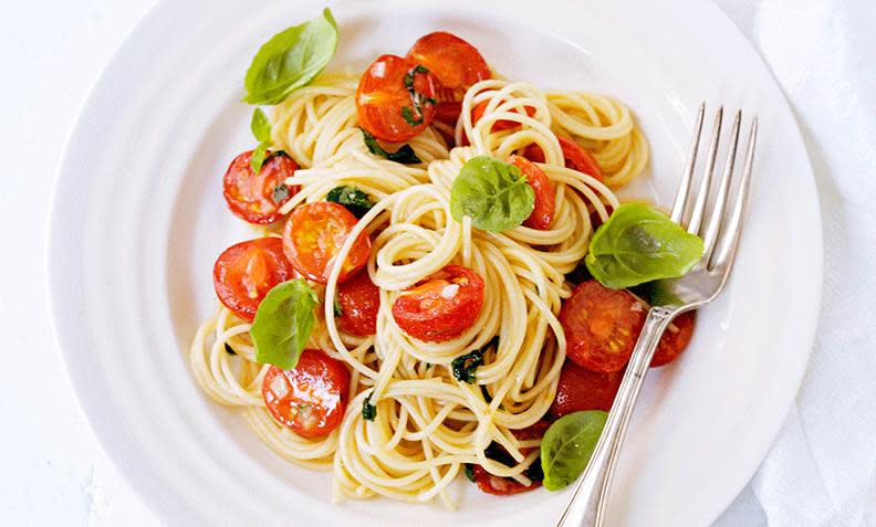 Spagetti med cherrytomater og basilikum, på hvit tallerken, med gaffel ved siden av.
