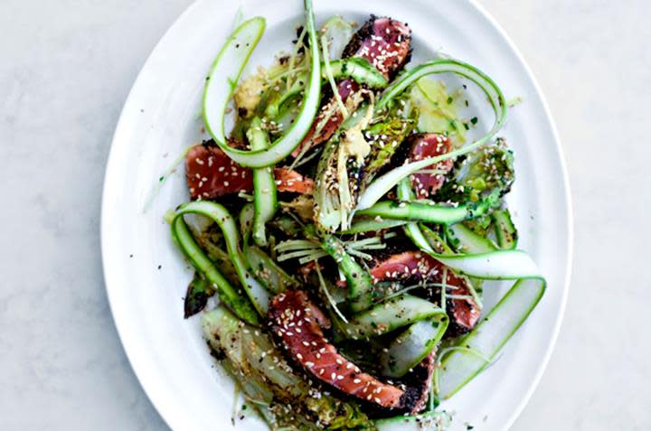 Ørret tataki med stekt hjertesalat og asparges, anrettet på hvitt ovalt serveringsfat. Hvit bakgrunn.