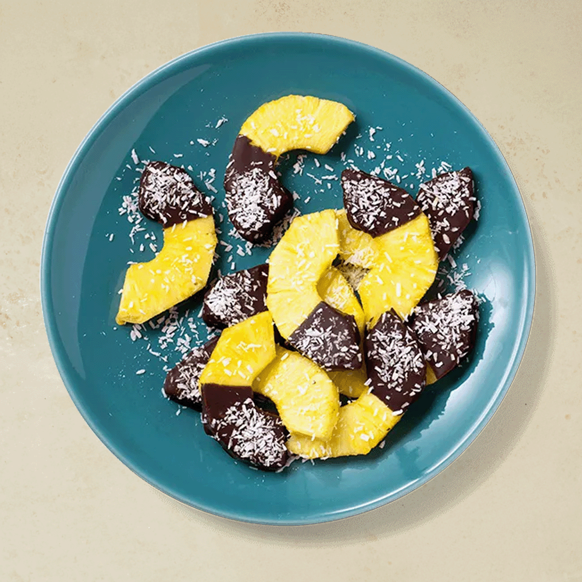 Ananas med sjokolade, delt i skiver og overstrødd med kokosmasse, servert på blå tallerken.