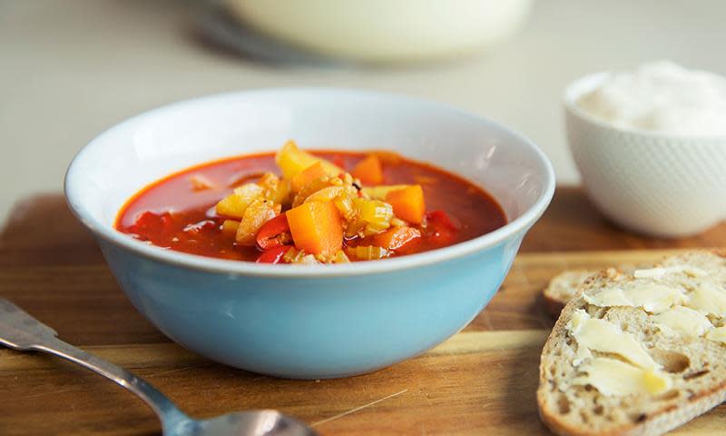 Rask gulasj med kjøttdeig, rød suppe med grønnsaker i hvit og blå skål, på trefjøl. Brød med smør ved siden av.