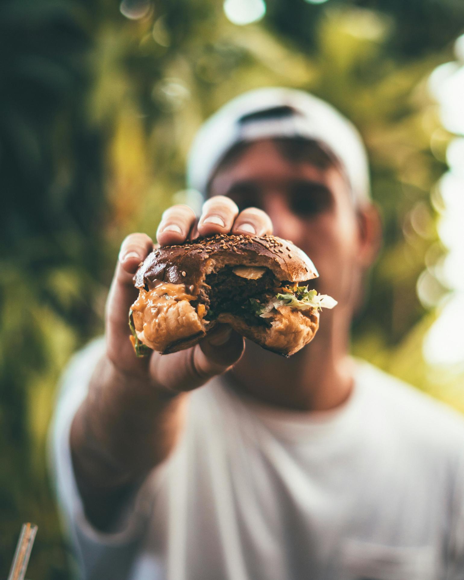 Mann som står ute og viser en grillet burger til kameraet