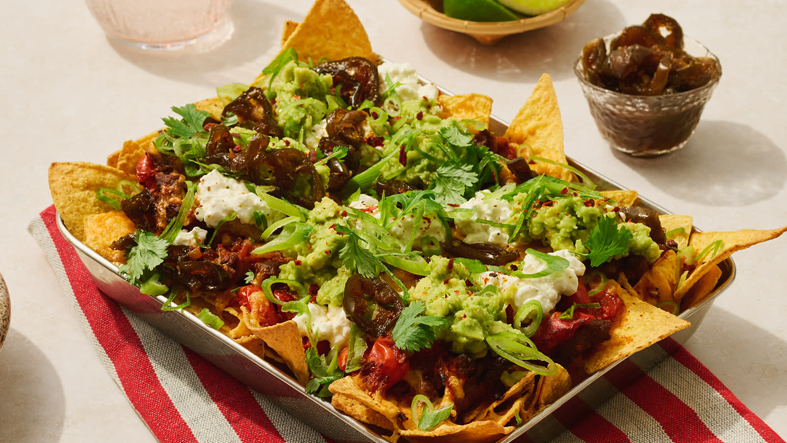 Loaded nachos med kjøtt, jalapeños, guacamole og cottage cheese servert i ildfast form på rødstripet kjøkkenserviett.