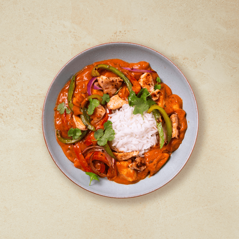 Tikka masala kyllinggryte med grønnsaker og ris, i en grå skål med rød kant. Fersk koriander på toppen.