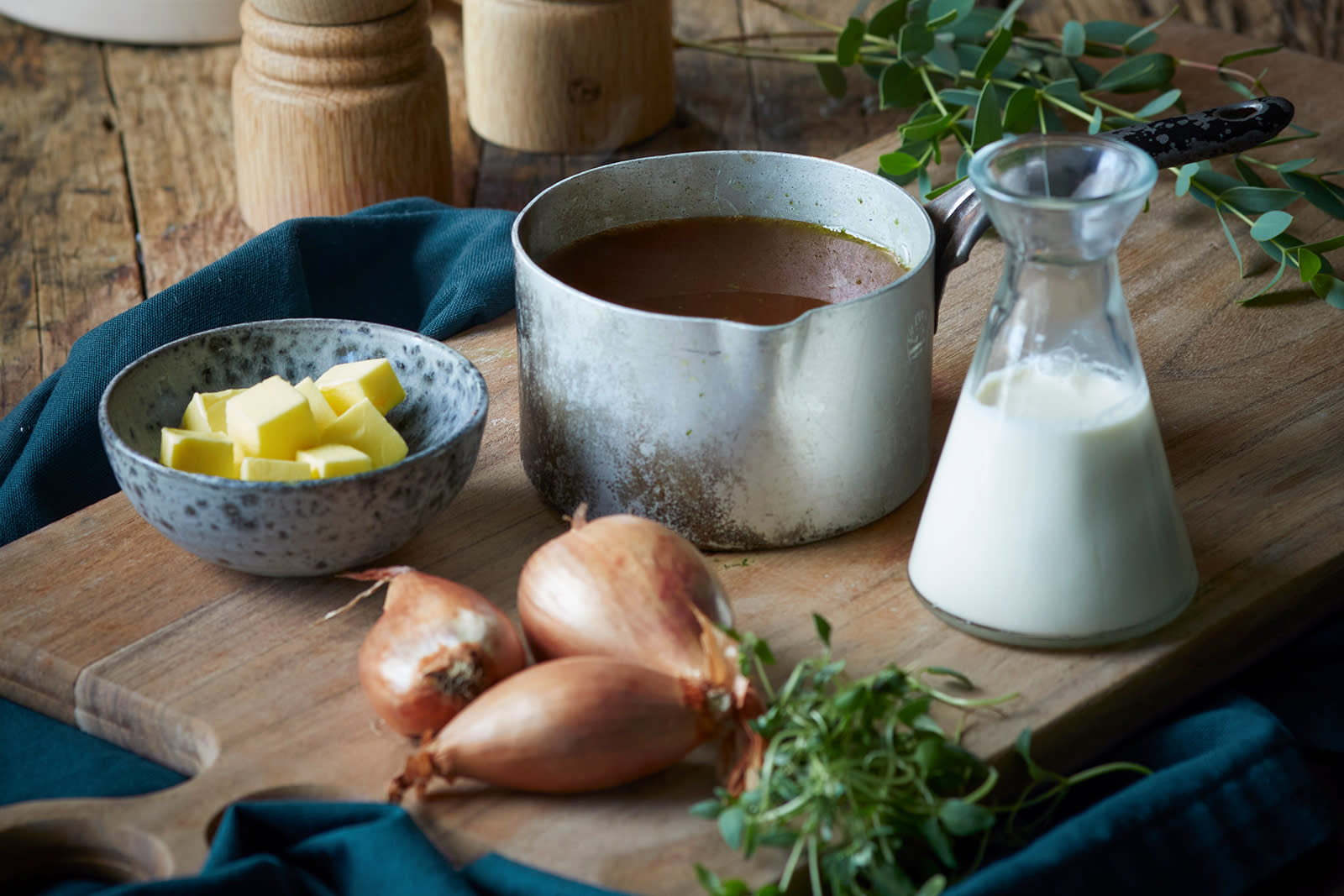Saus til ribbe servert i liten metallkasserolle på trefjøl med en liten skål smør, en liten karaffel kremfløte, sjalottløk og urter rundt.