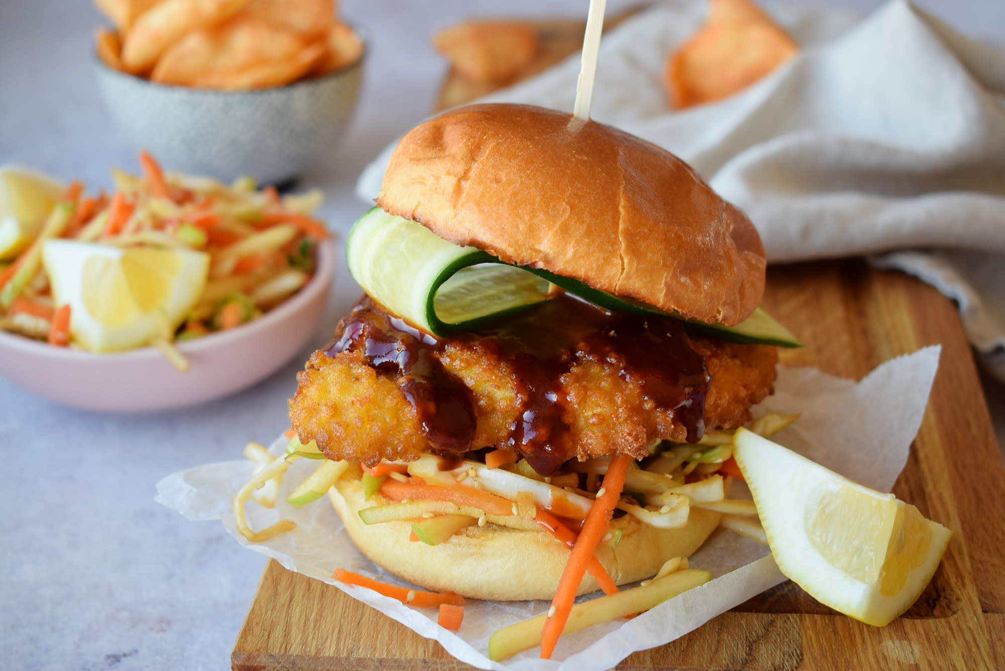 Japanskinspirert kyllingburger med coleslaw, grillet Coop Grill Perfekt Crispy kyllingburger, brioche burgerbrød, agurk og barbecue saus. Coleslaw og chips i bakgrunnen.