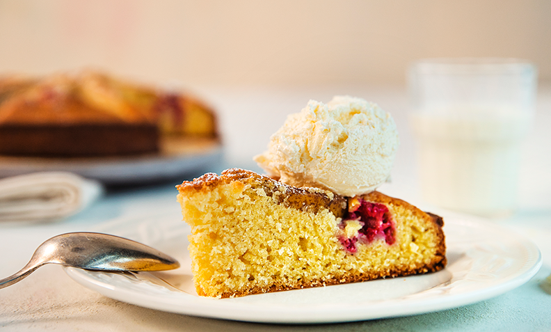 Et stykke Likevektskake, en kake laget av like deler egg, mel, smør og sukker, med pære og bringebær. Servert på en hvit tallerken, med en kule vaniljeis på toppen, og resten av kaken i bakgrunnen.
