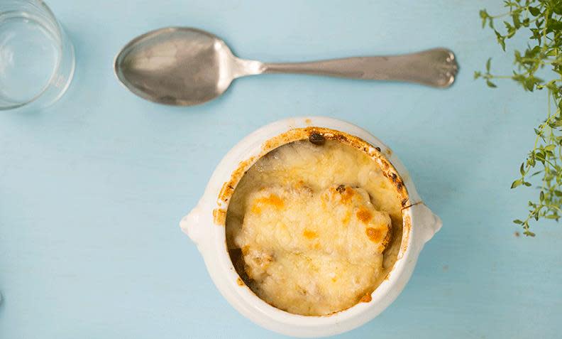 Gratinert fransk løksuppe i hvit suppeskål, på lyseblå bakgrunn. Fersk timian på siden.