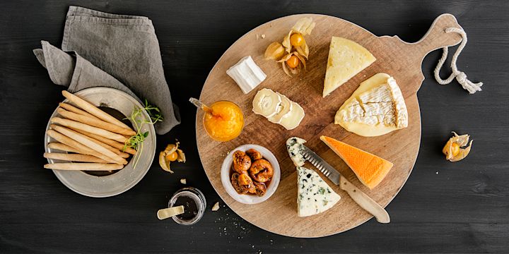 Fjøl med fem ulike oster, tørkede fikener, physalis, aprikosmarmelade og brødpinner. 