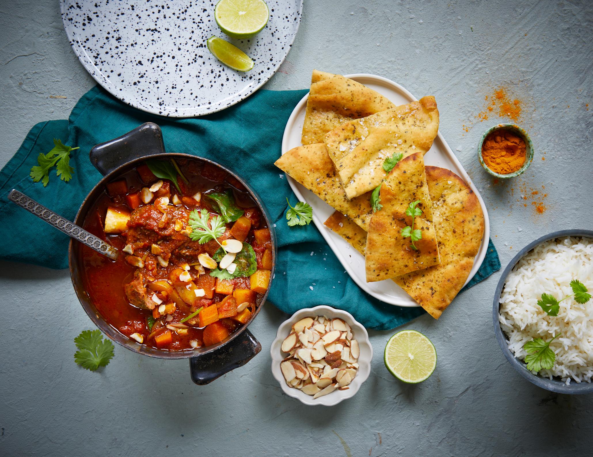 Indisk curry i en gryte med nanbrød og ris servert på siden