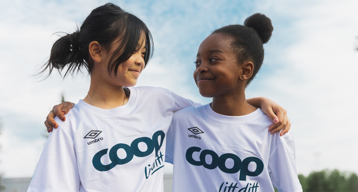 Bilde av to jenter i hvit Coop drakt som holder rundt hverandre og smiler til hverandre