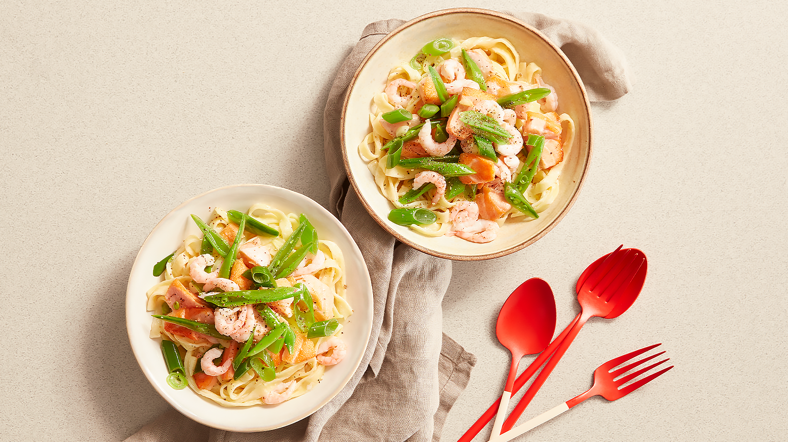 Kremet reke- og laksepasta i boller med rødt bestikk ved siden av