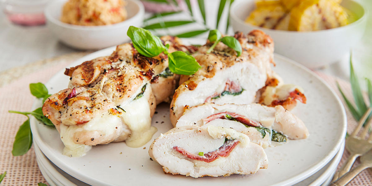 Fylt kyllingfilet med mozzarella og spekeskinke, toppet med basilikum og servert på hvit tallerken.